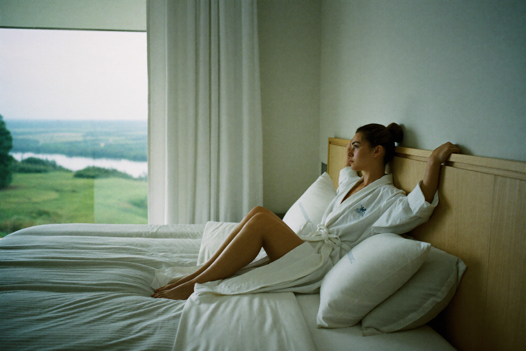 A woman waking rested in a hotel bedroom, looking out at a quiet landscape