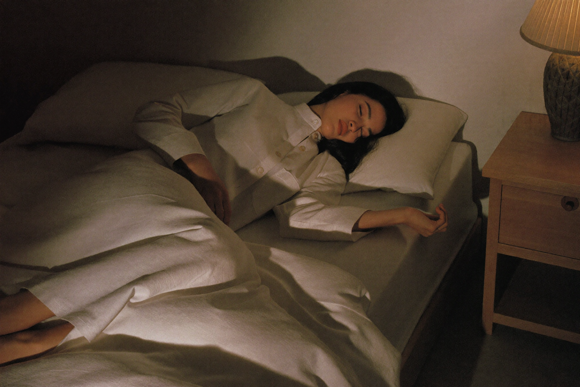 A woman asleep in linen pyjamas with one leg outside the duvet to cool down