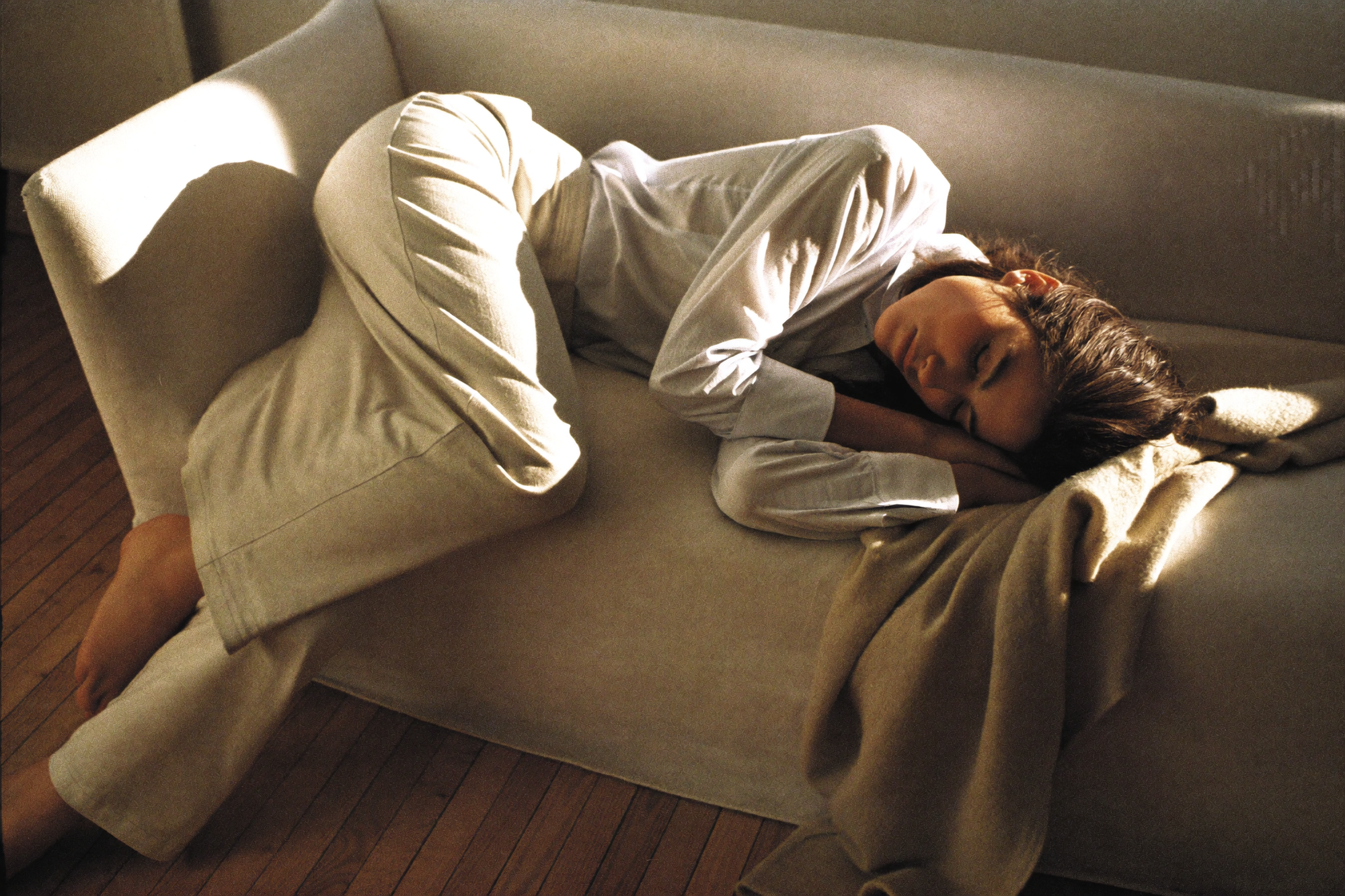 A woman asleep on a sofa in the afternoon under a light wool throw