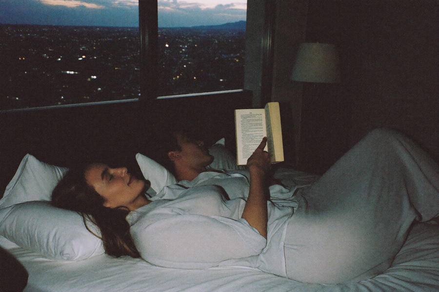 A couple settled in bed at nine in the evening, city windows glowing beyond