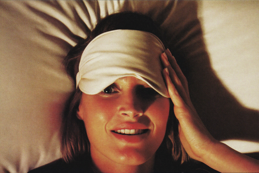 A woman pushing a silk sleep mask up onto her forehead as she wakes