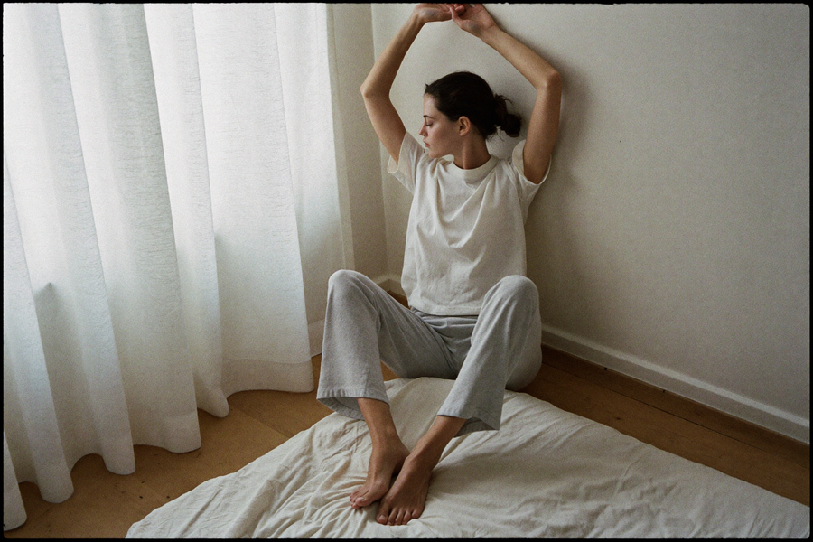 A woman stretching her arms overhead just after waking, in flat morning light