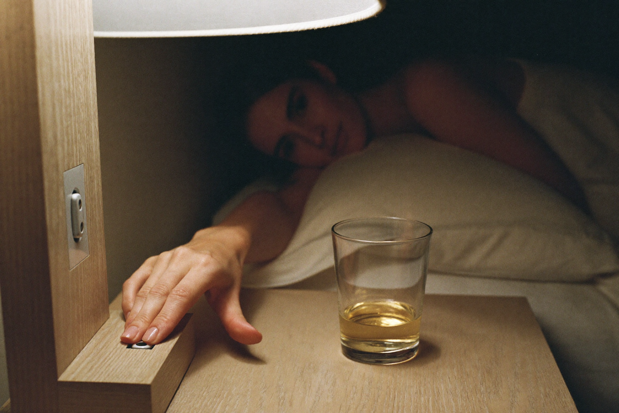 A hand reaching for the bedside lamp switch beside a glass of water