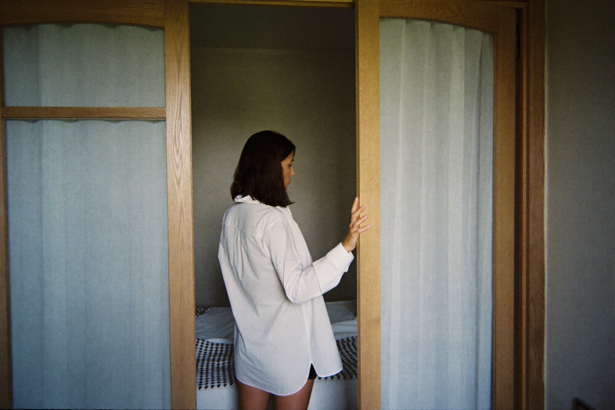 A woman pausing in the doorway of her bedroom, looking in at the made bed