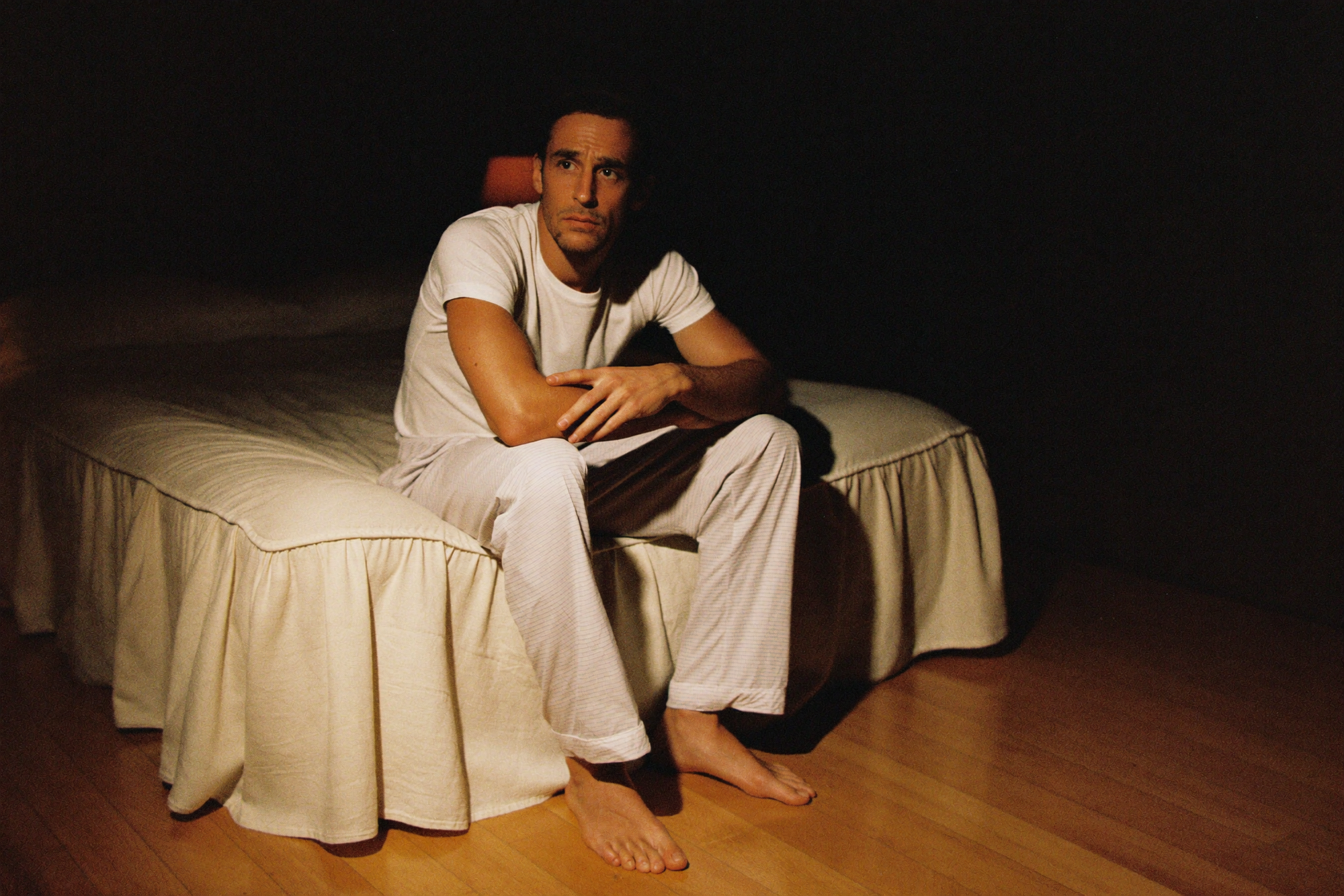 A man sitting on the edge of his bed in the dark after giving up on sleep