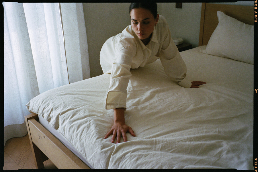 A woman smoothing a heavy linen duvet across a beautifully made bed
