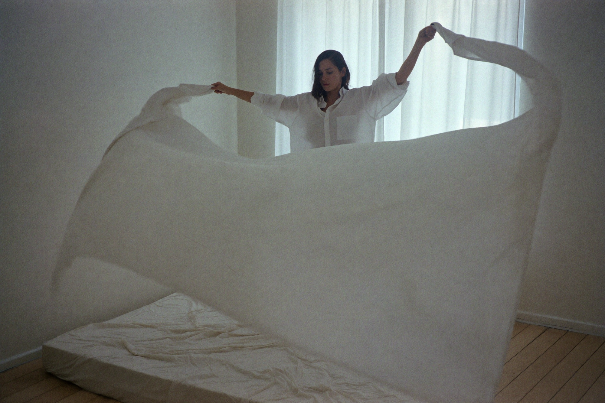 A woman shaking a clean white sheet out over a bare mattress