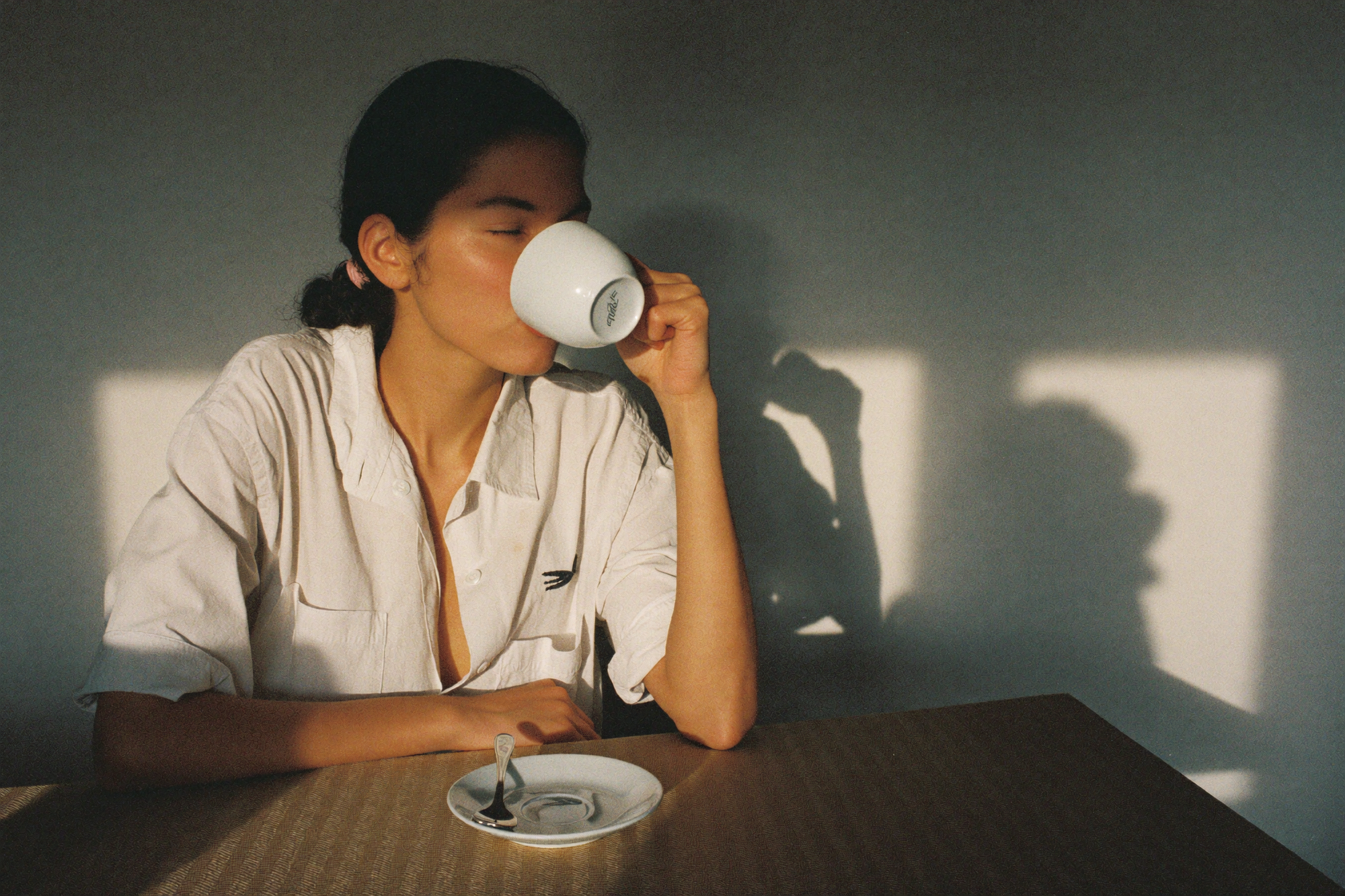 A woman drinking coffee in low late-afternoon sun, her shadow thrown long