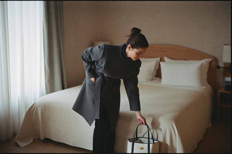 A woman setting a bag down at the foot of an immaculately made hotel bed