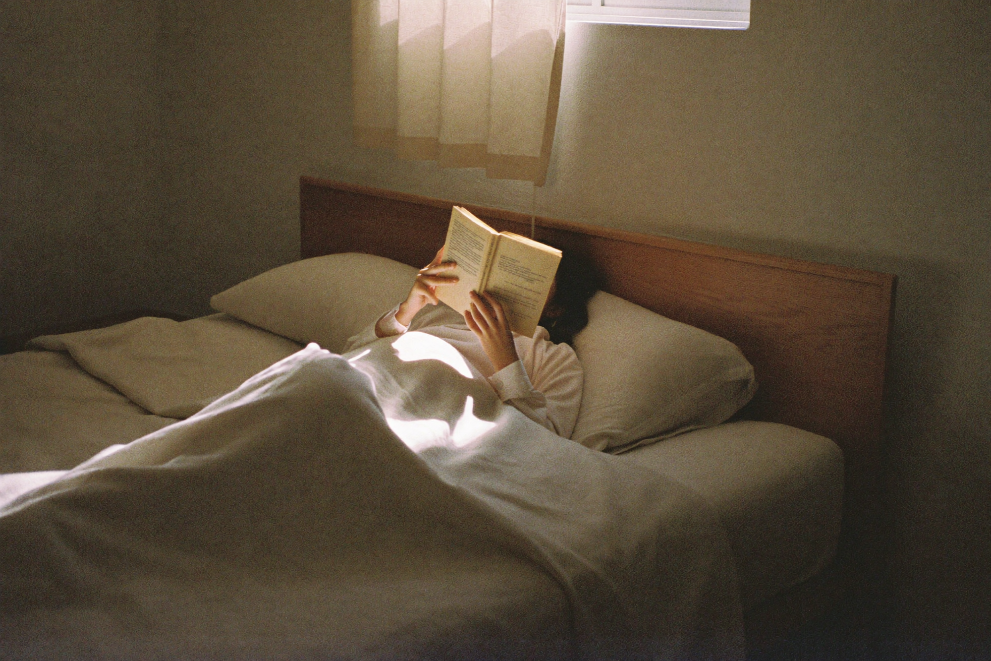 A woman reading in bed in the middle of the afternoon