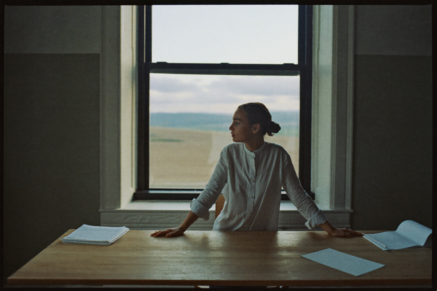 A woman standing at a bare desk in the first grey light of morning