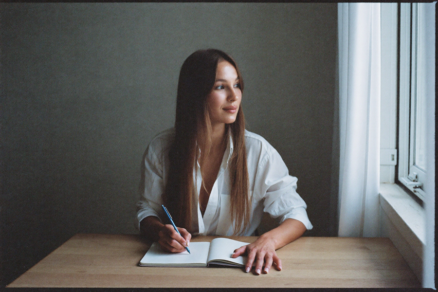 A woman writing in a notebook by a window early in the morning
