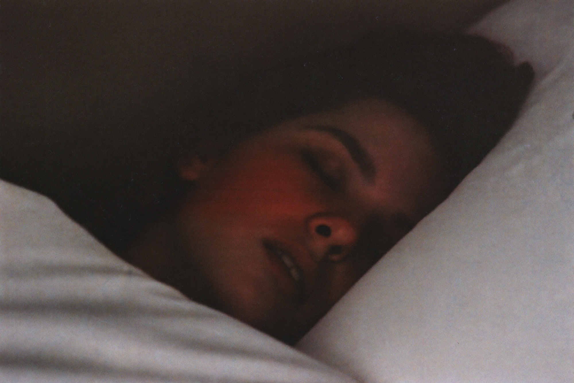 A close view of a woman deeply asleep, her face turned into a white pillow