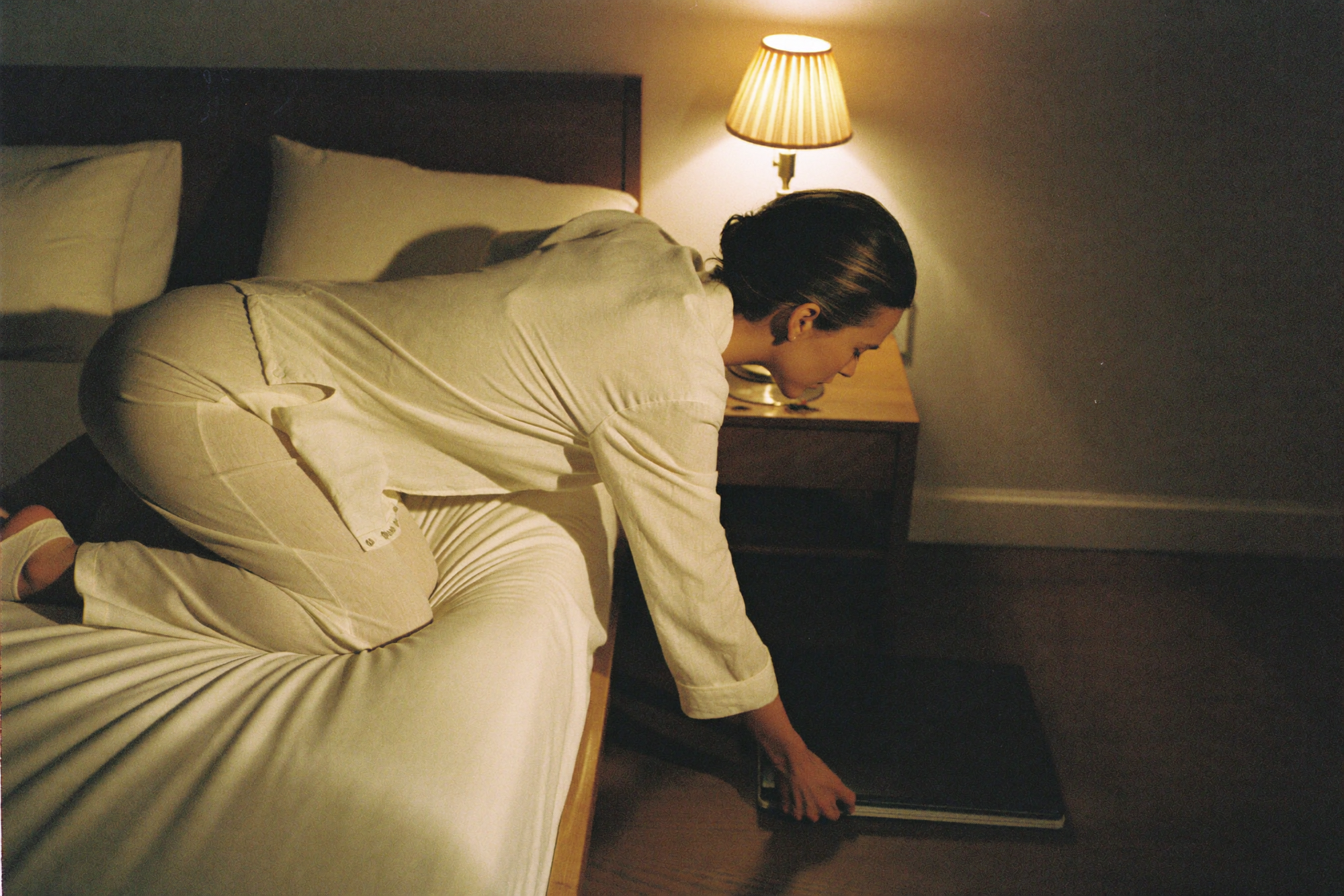 A woman clearing work off her bed before sleep by lamplight