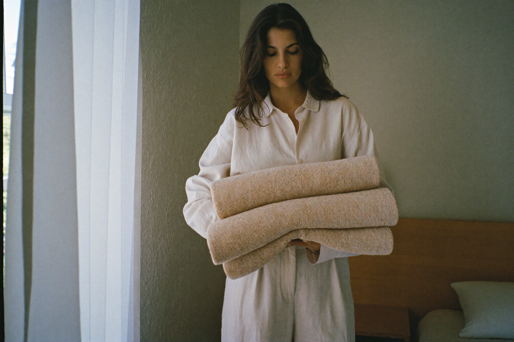 A woman holding a single folded wool blanket in an almost bare bedroom