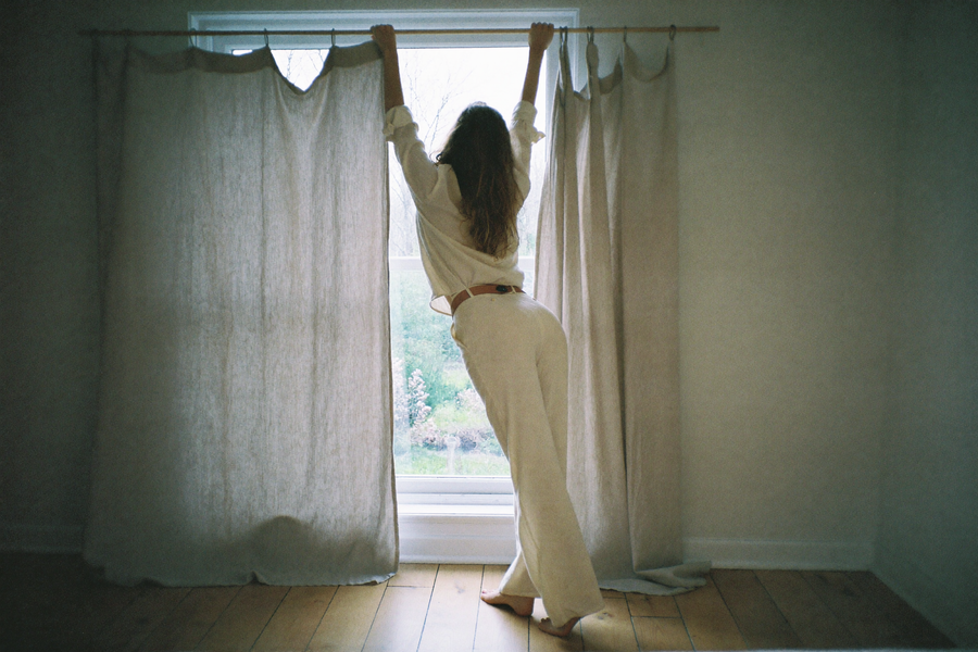 A woman hanging a heavy linen curtain above a bedroom window