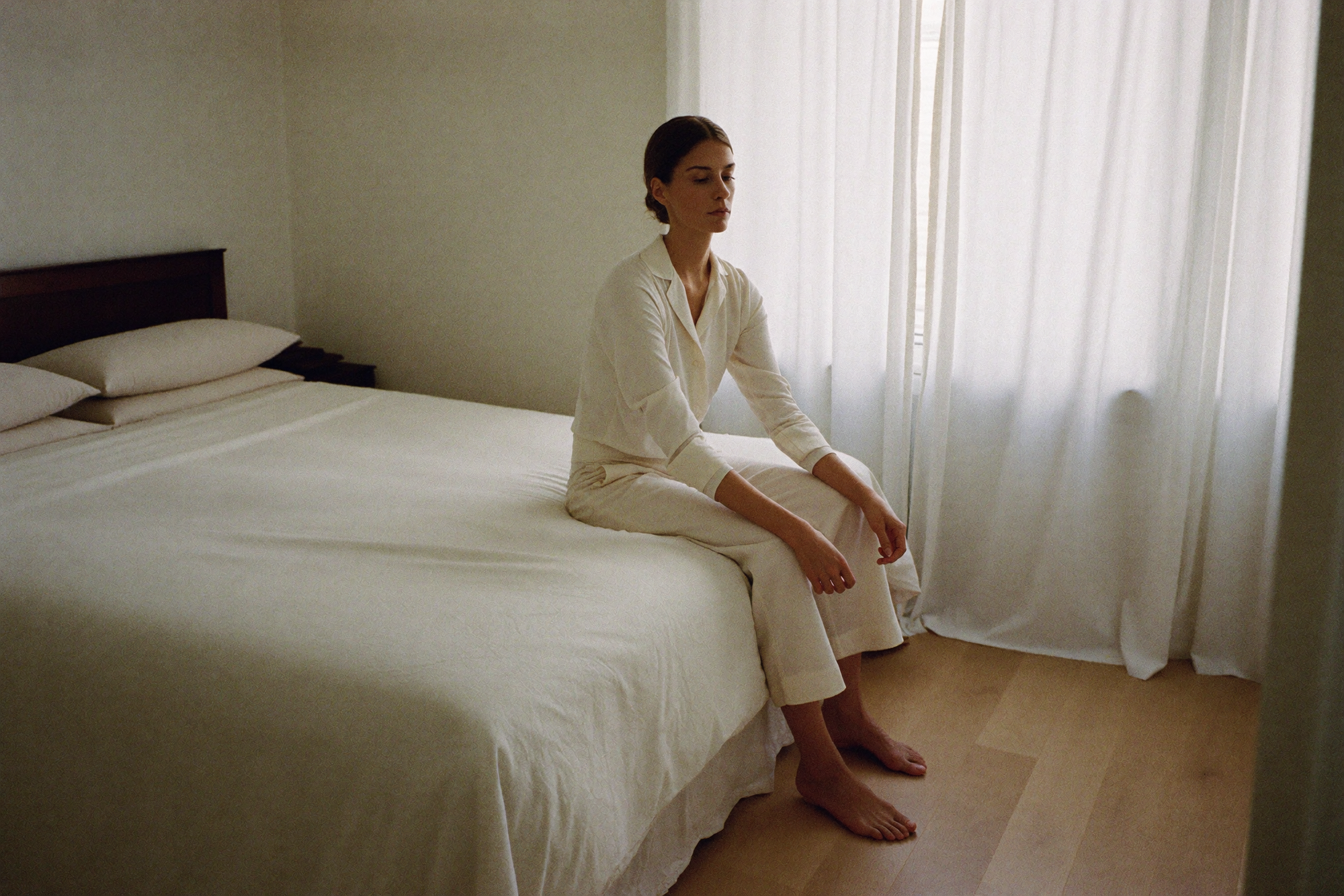 A woman sitting cross-legged on her made bed with her eyes closed