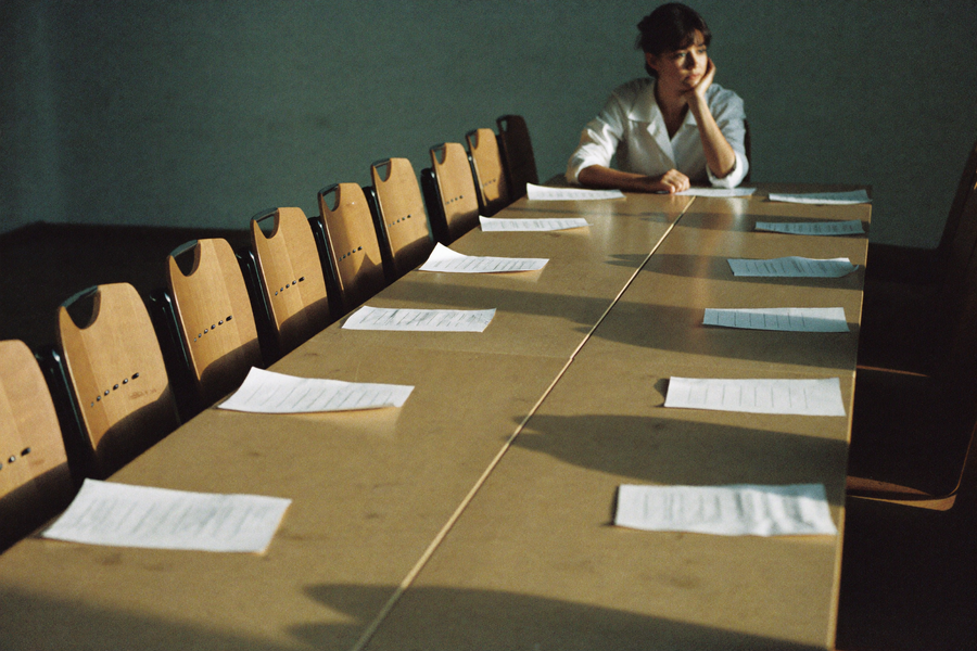 One woman left at the end of a long empty meeting table late in the afternoon