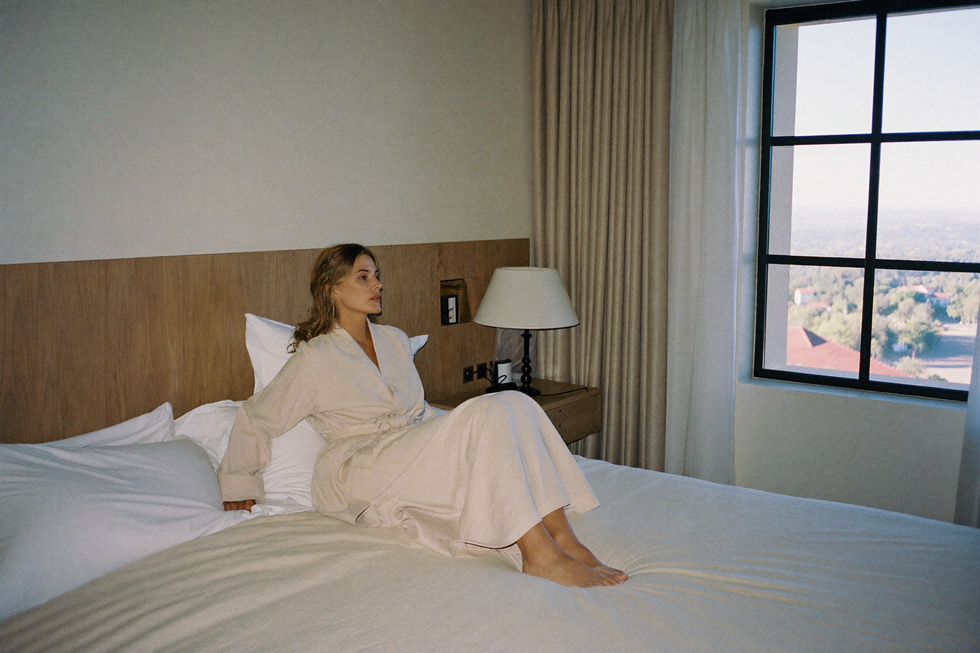 A woman waking rested in a hotel bedroom looking out at a quiet landscape