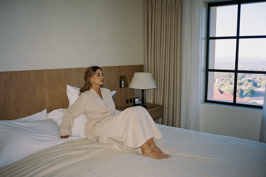 A woman waking rested in a hotel bedroom looking out at a quiet landscape