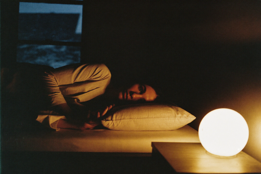 A woman waking as a wide amber glow rises from a round light on the nightstand