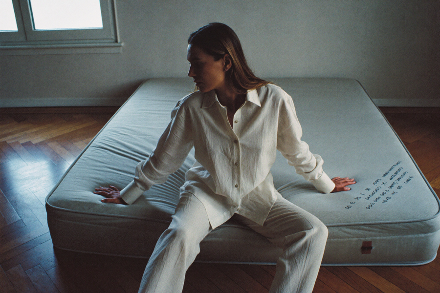 A woman sitting alone on a bare mattress in an otherwise empty room